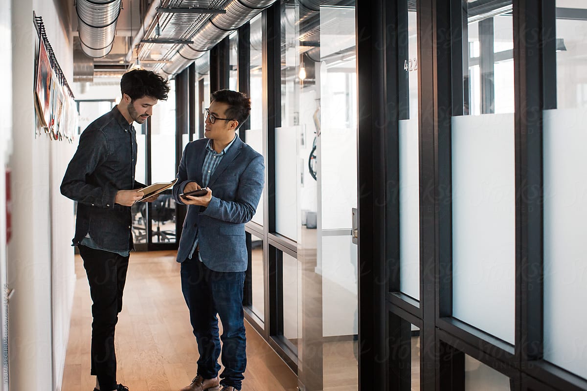 Two Young Businessmen Standing in Bright Modern Office Corridor