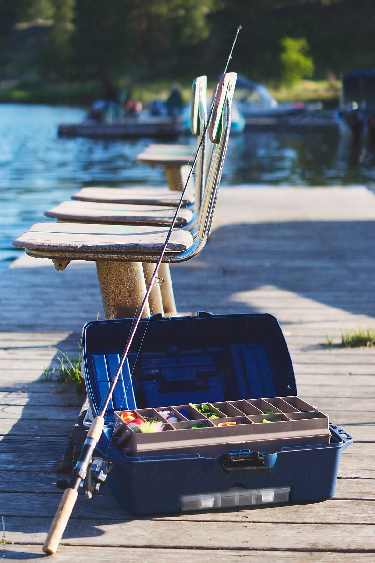 A Fishing Pole Leans Against A Tackle Box Next To Chairs On A Fishing Dock  by Stocksy Contributor Tana Teel - Stocksy