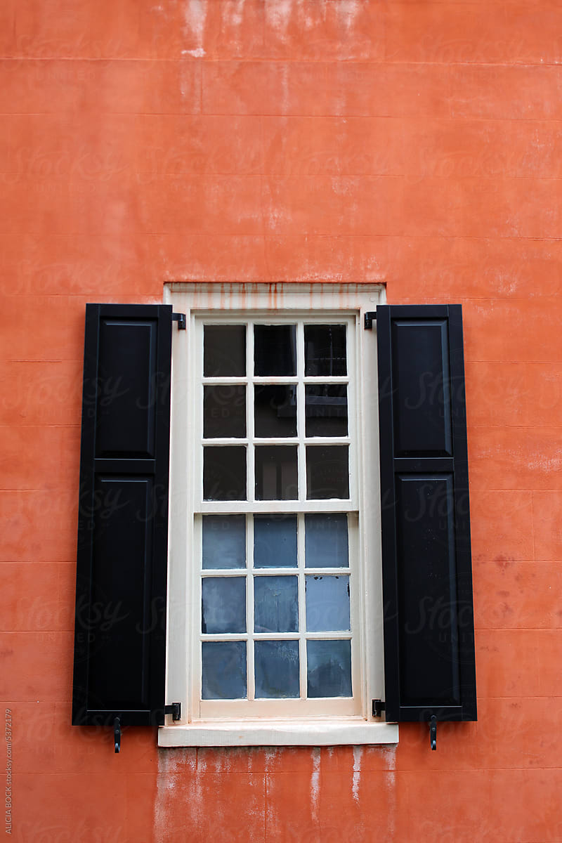 A Window With Black Shutters On An Orange Building