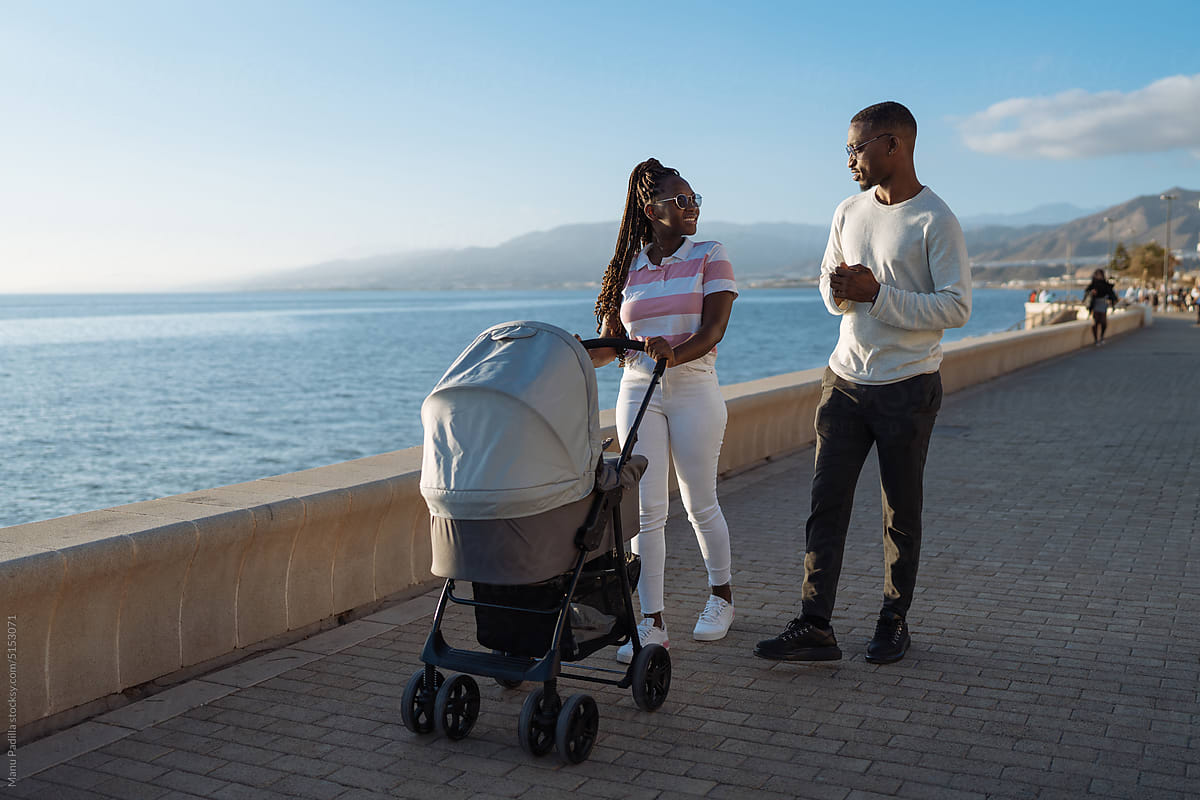 Black family strolling with baby carriage on embankment