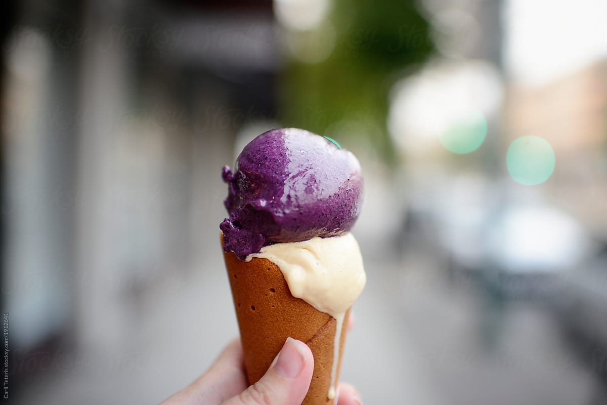 Hand holding double scoop ice cream cone on the street