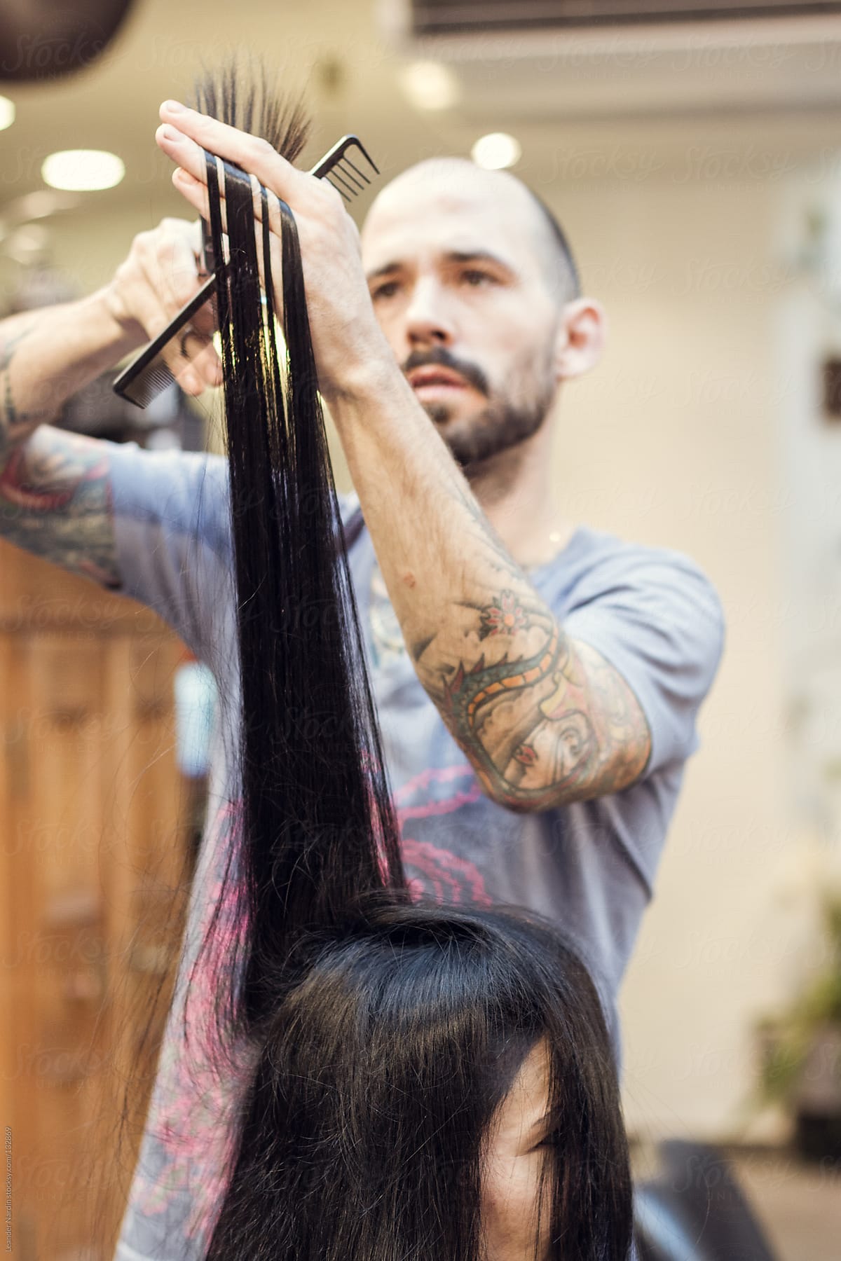 woman is getting her long hair cut by a tattoed hairdresser