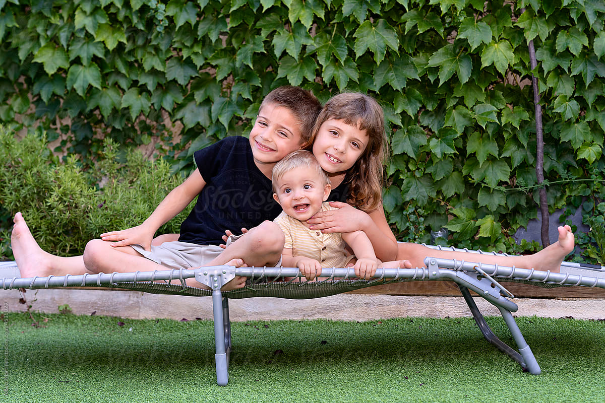 Happy siblings gently embracing on camp bed in yard
