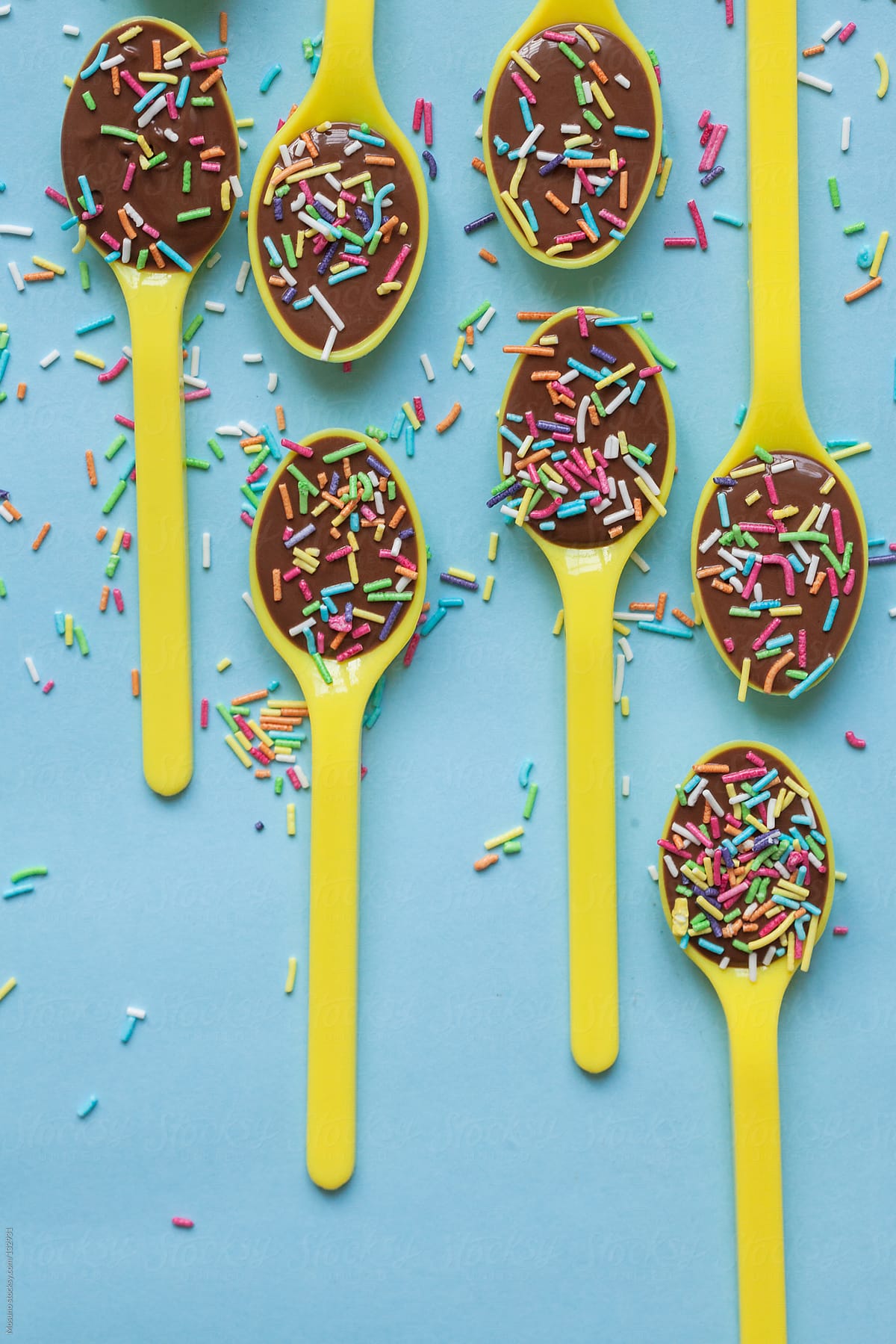 Chocolate pudding in yellow spoons with colorful sprinkles.