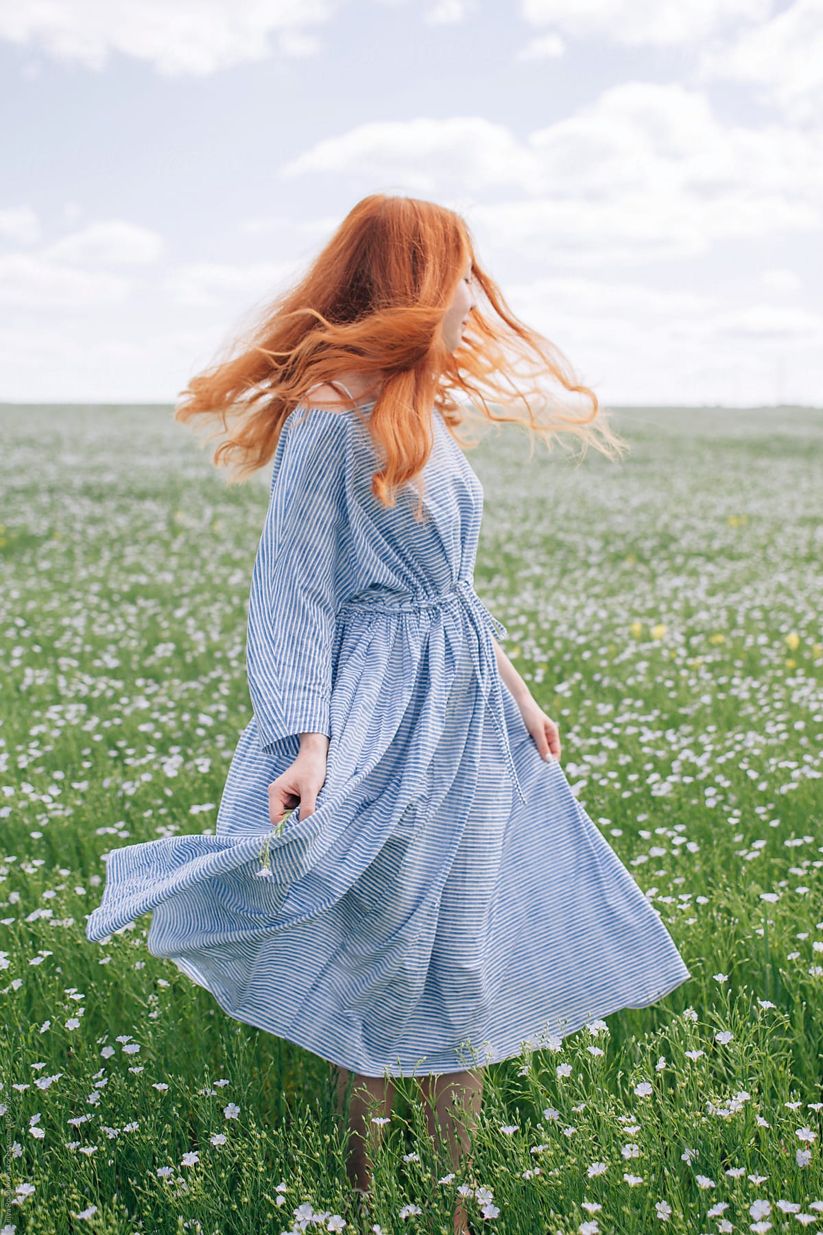 Young redhead woman in blue dress swirl in the summer meadow