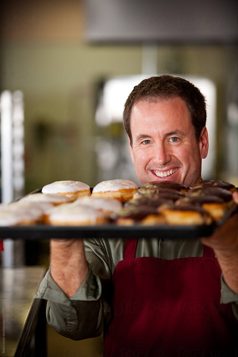 Bakery: Baker Peeks Over Tray of Donuts