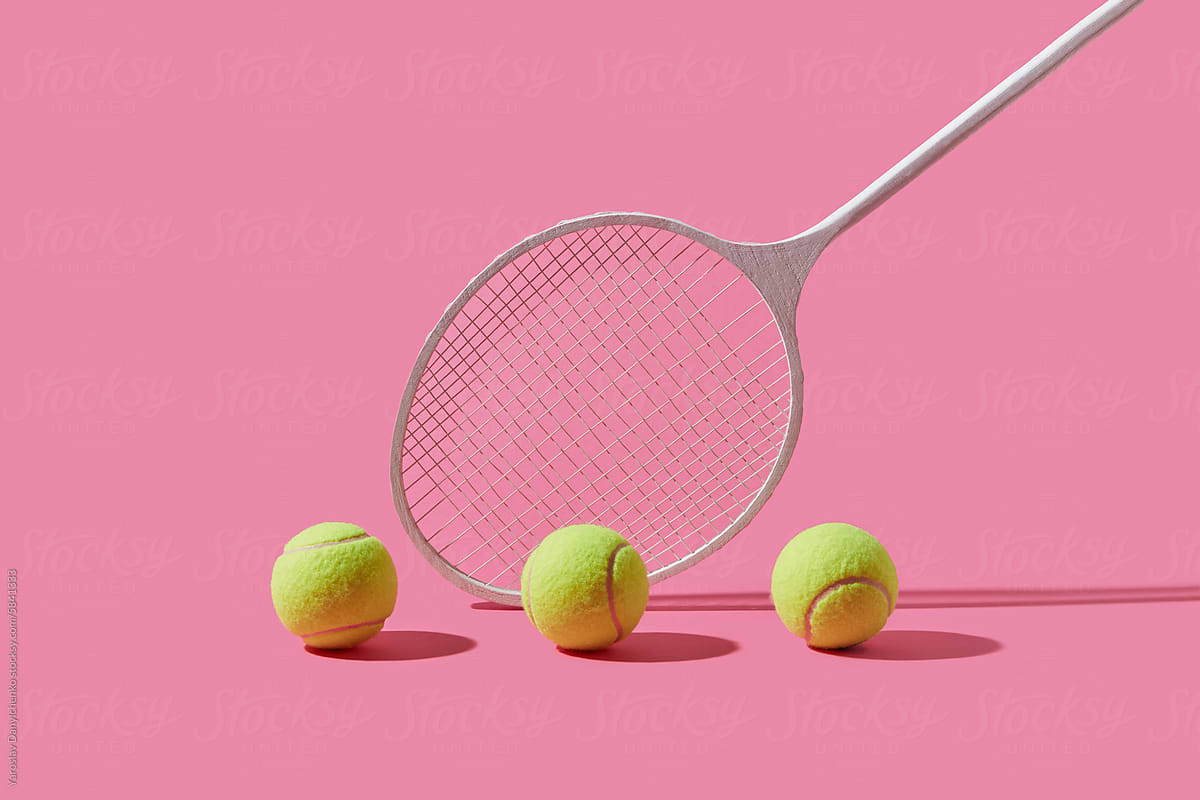 Tennis racket and three yellow balls over pink studio background