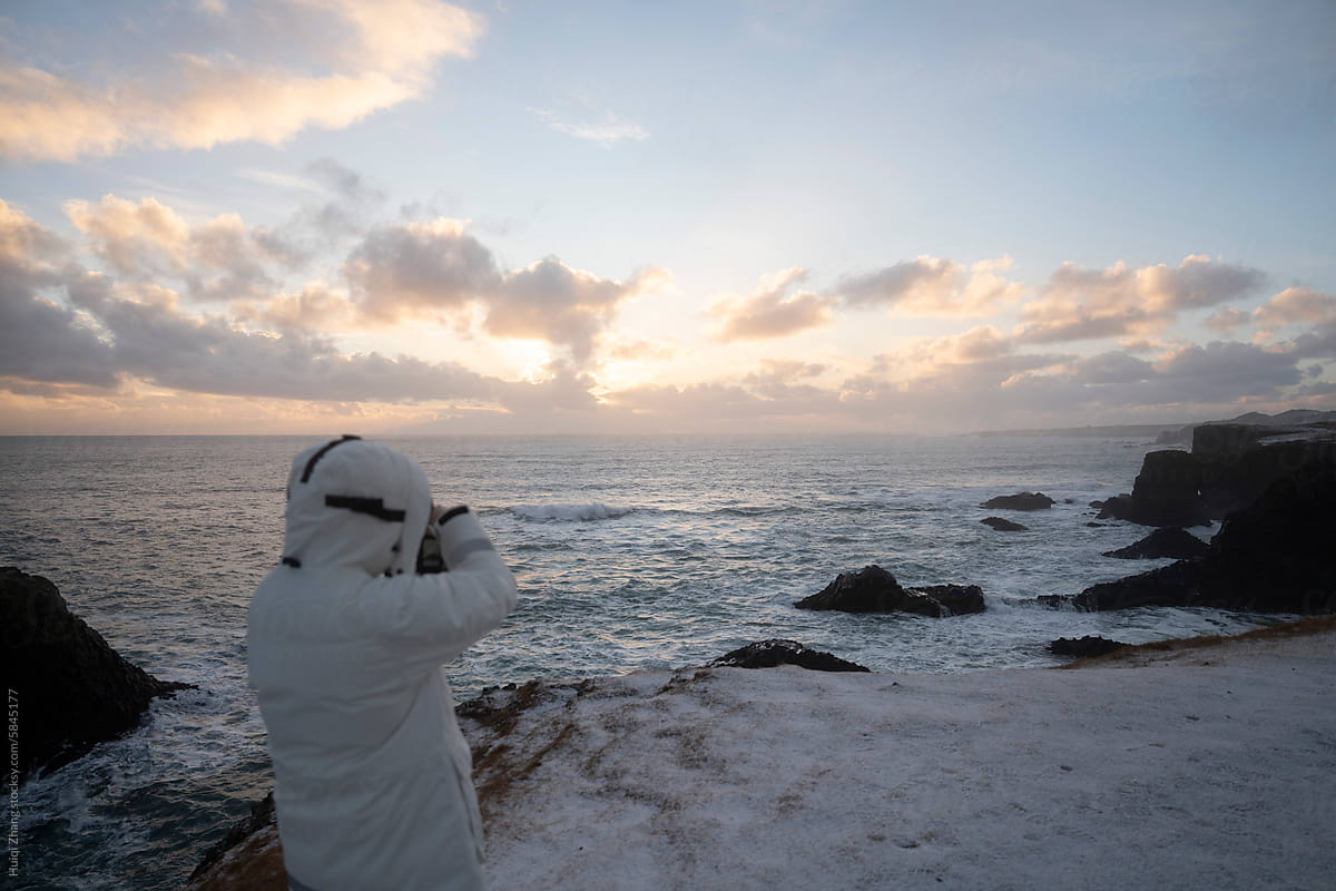 A photographer faces the sea in Iceland before sunset in winter.