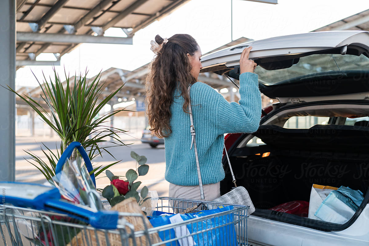 Woman opening car trunk with shopping cart