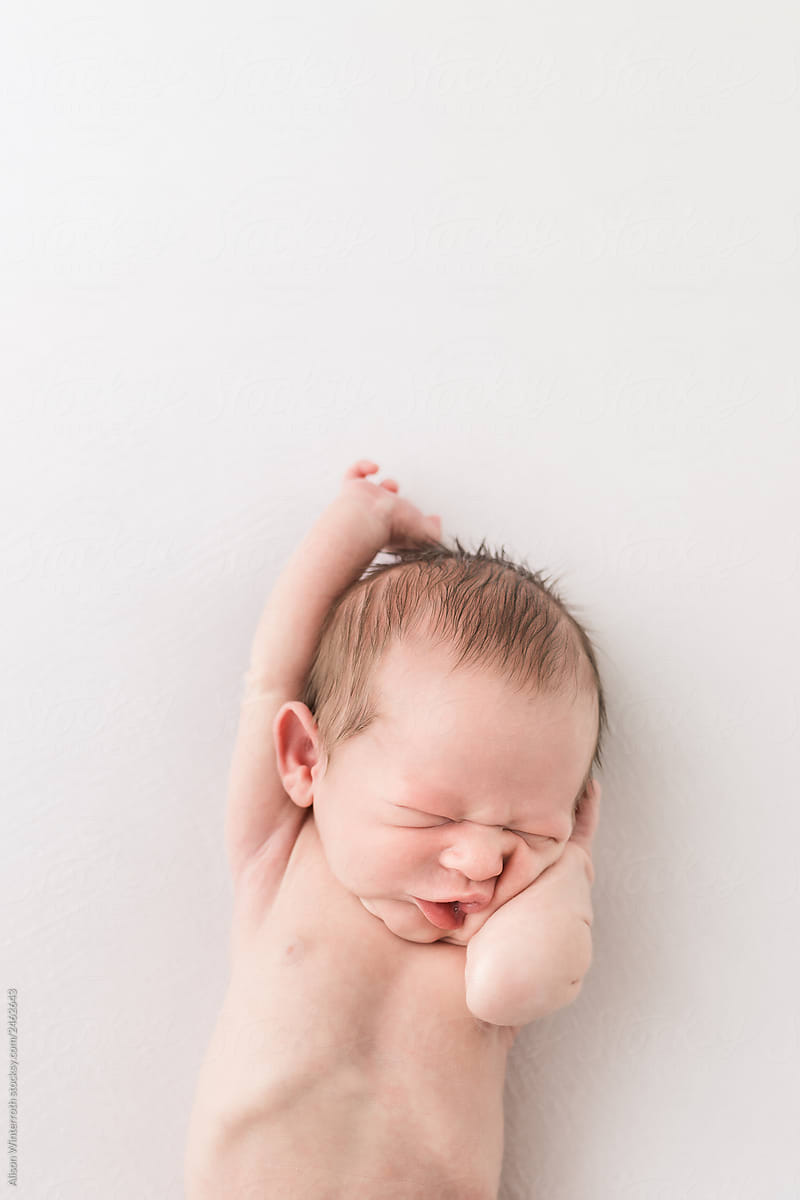 A Newborn Baby Making A Crazy Face While Laying on A White Backdrop