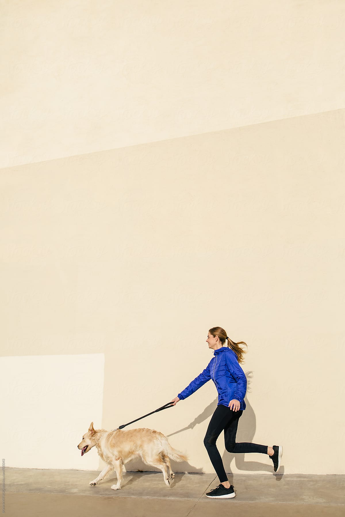 Side view of a woman running with her dog on the street.