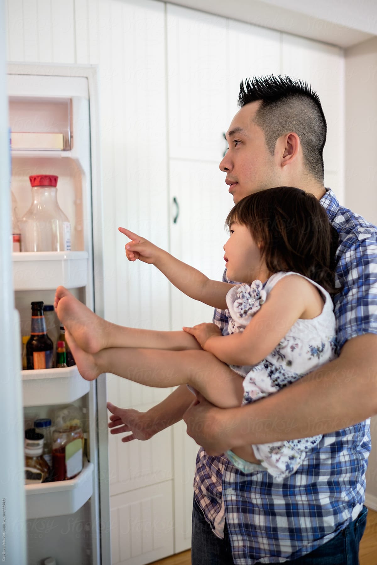 Little Asian girl looking into a refrigerator with her dad in the kitchen