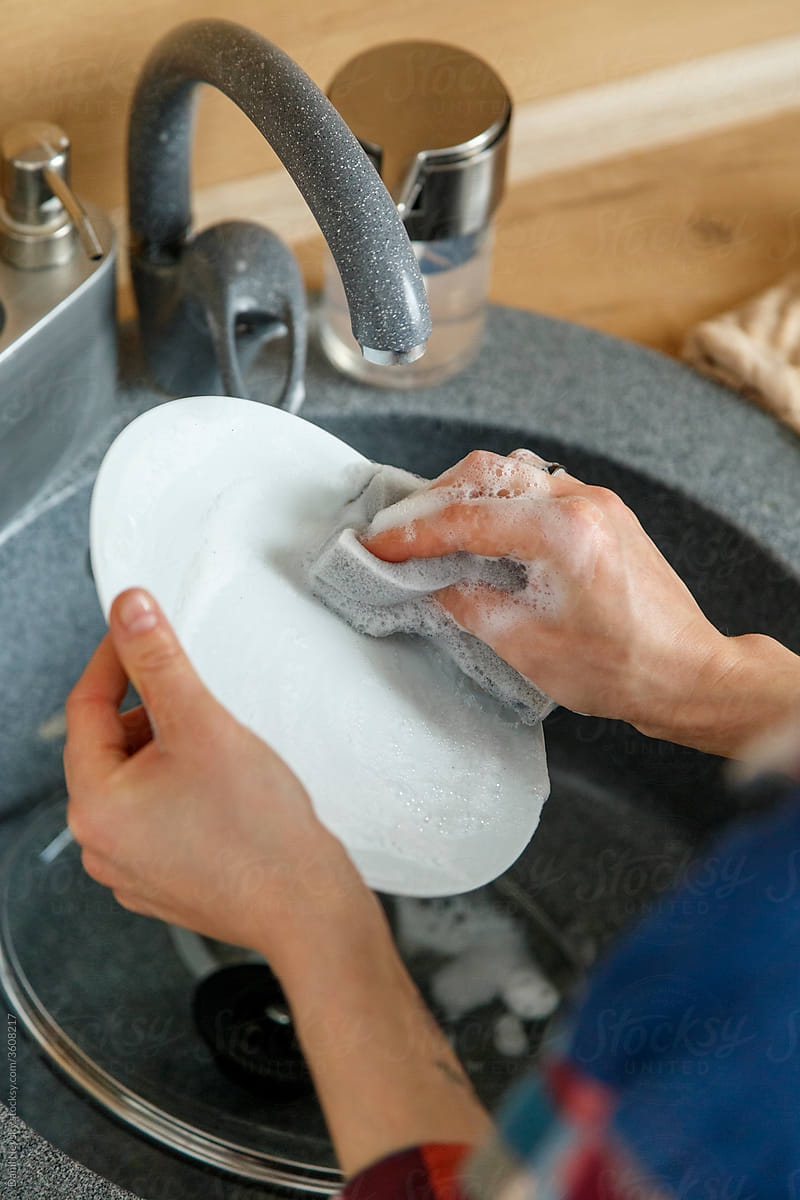 Unrecognizable housewife washing plate over sink