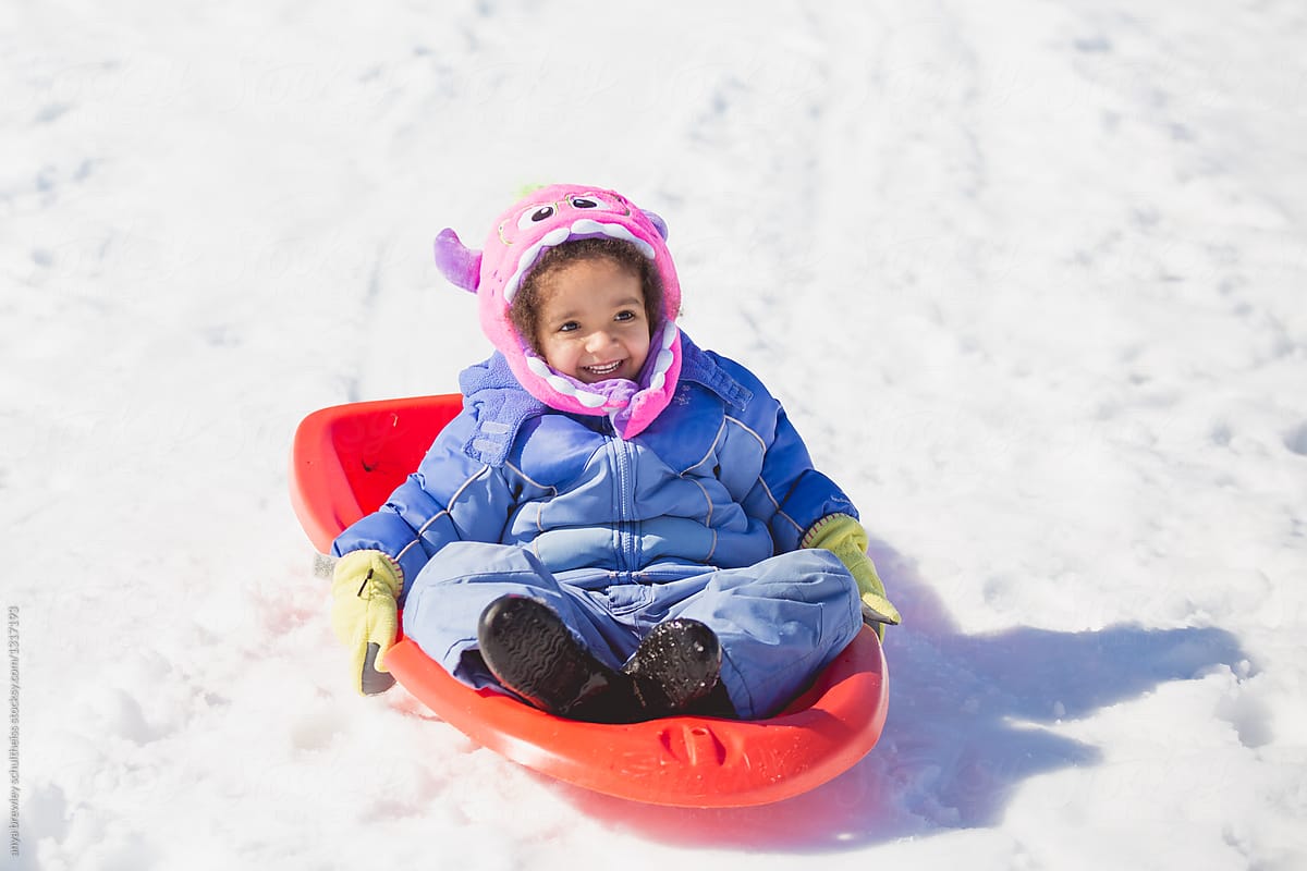 Toddler child happily sledding down a snowy hill