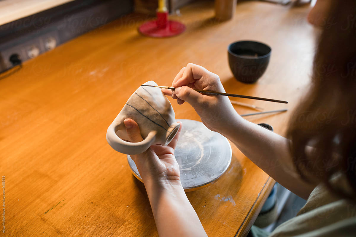 Young unrecognizable woman ceramist applying paint to clay mug