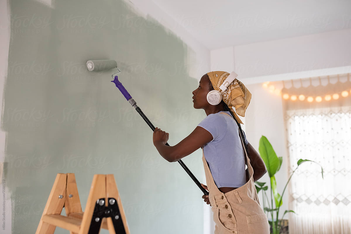 Black woman listening to music and painting wall
