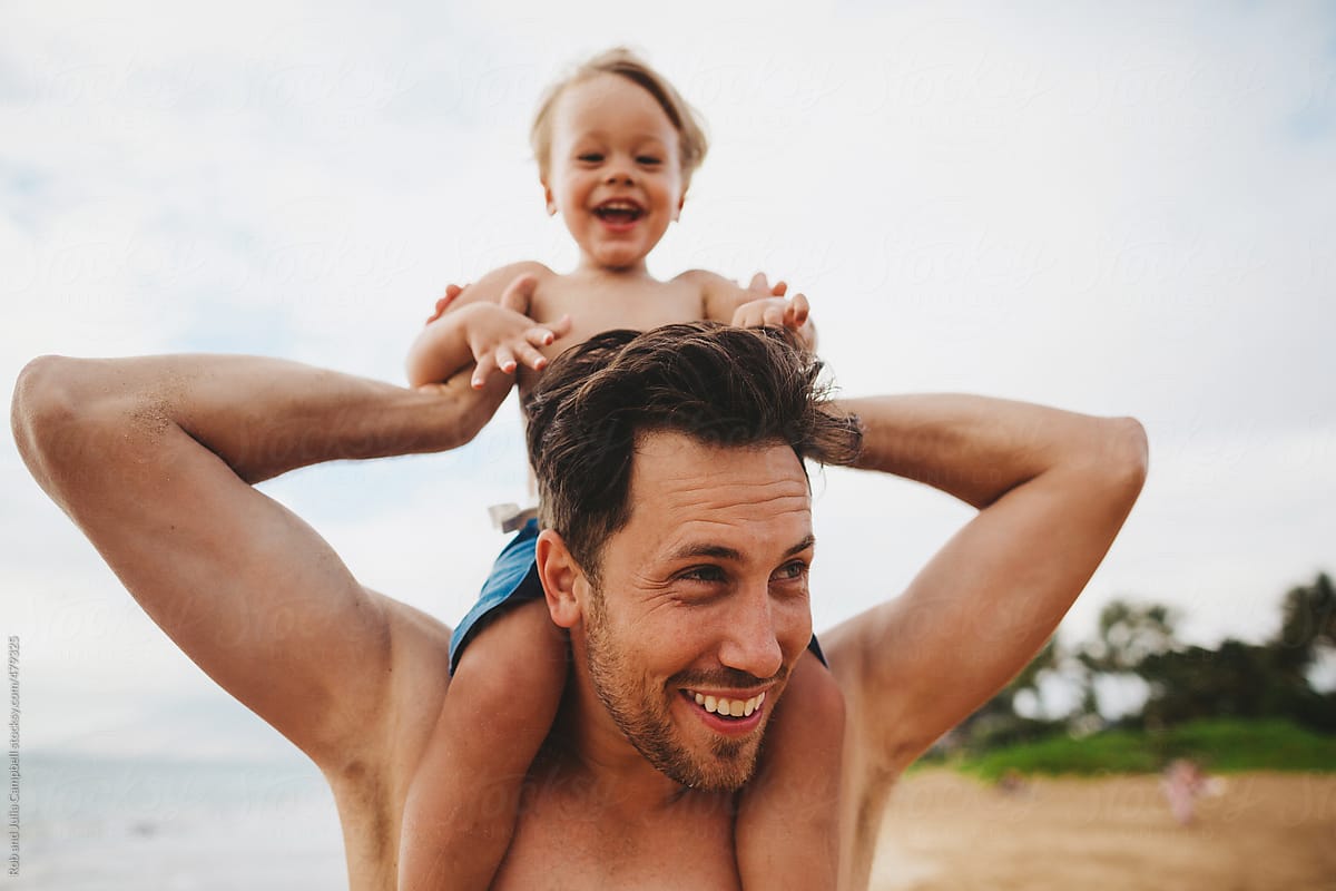 Young dad having fun with toddler son on tropical beach - kid pulling hair