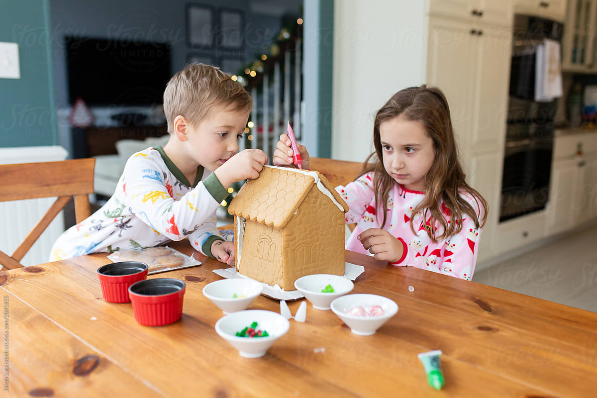Brother and sister decorating a gingerbread house for the holidays