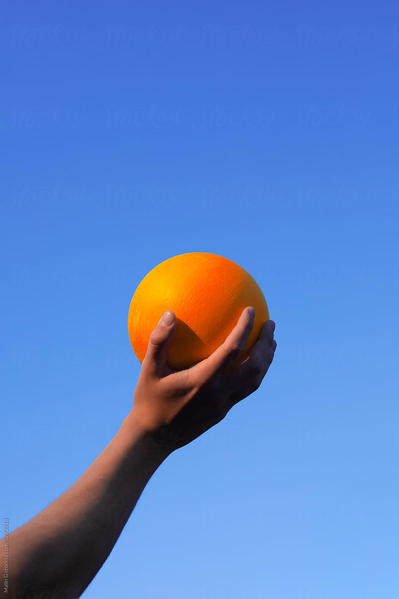 Hand holding a yellow ball and blue sky background