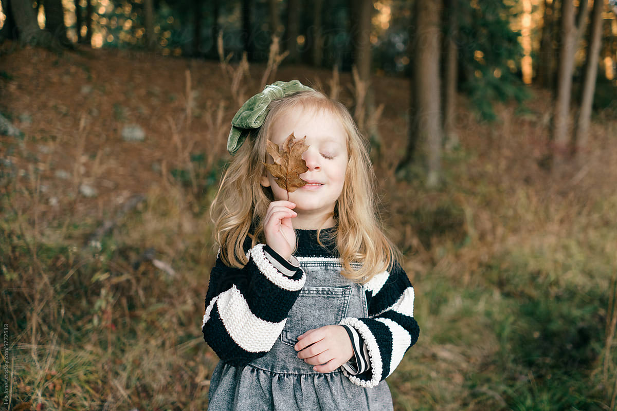 little  blonde/ginger girl holding a leaf in front of her eye