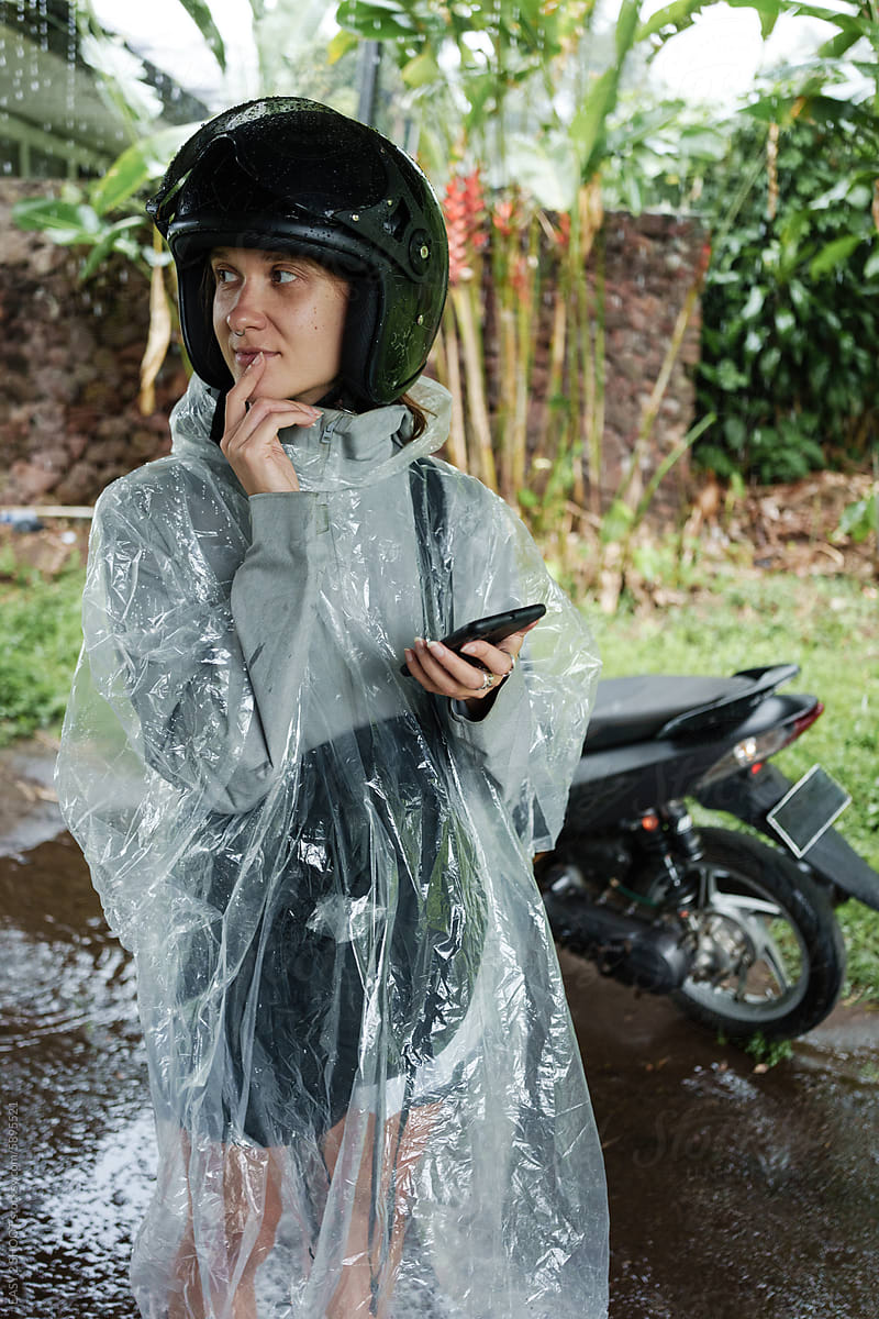 Smiling Person in Rain Gear Checking Phone Under Shelter