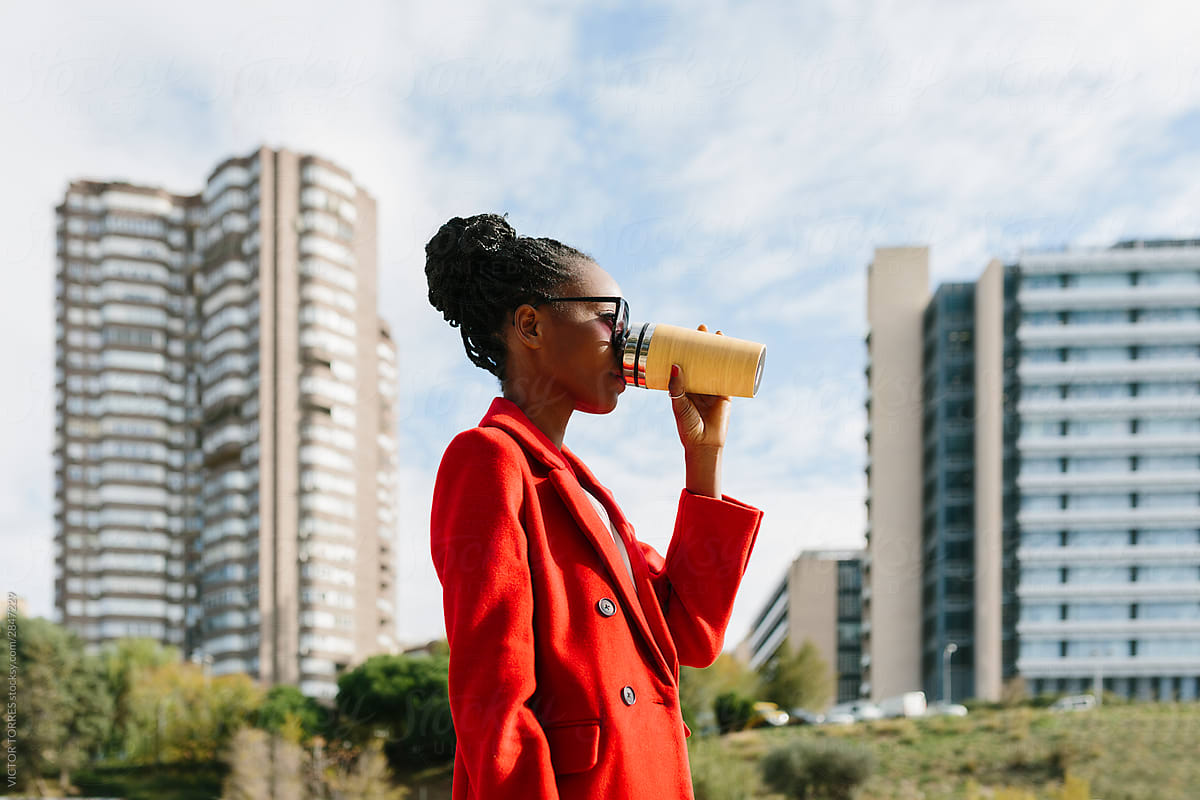 Thirsty black woman in sunglasses and coat drinking from bottle