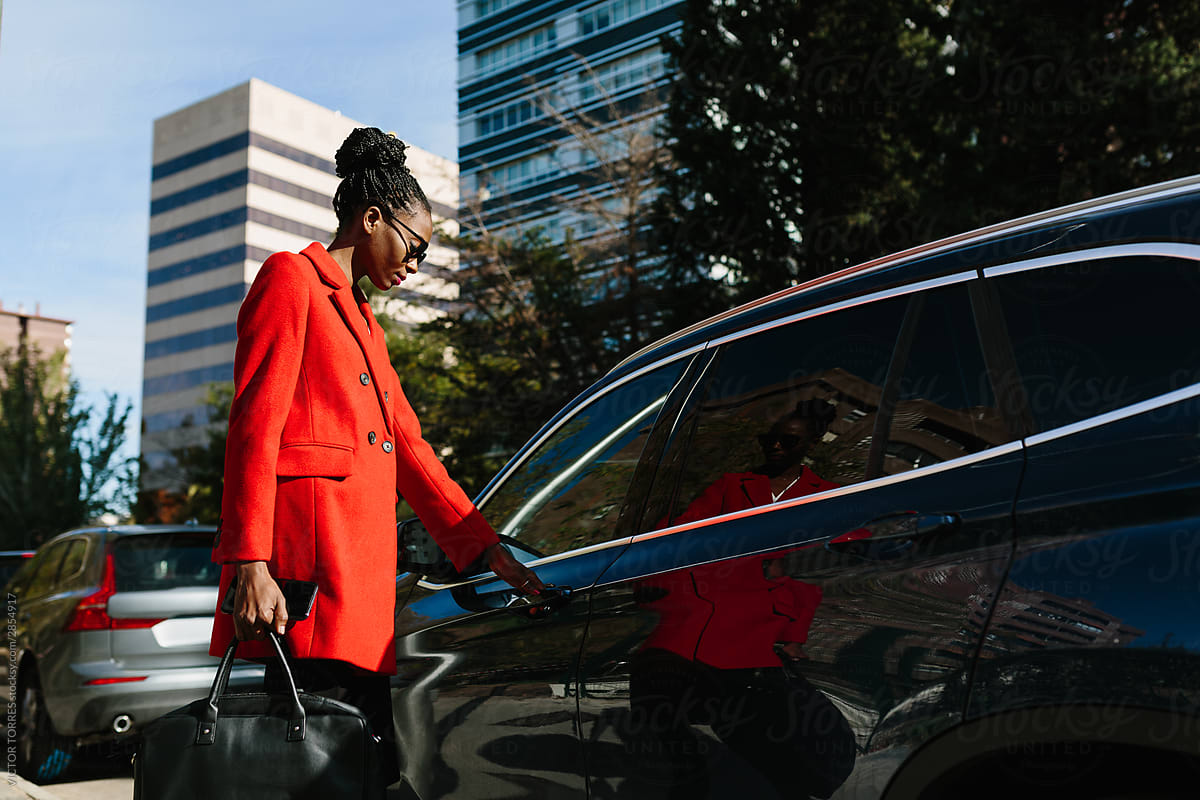 Active black woman in sunglasses and coat opening car door in street