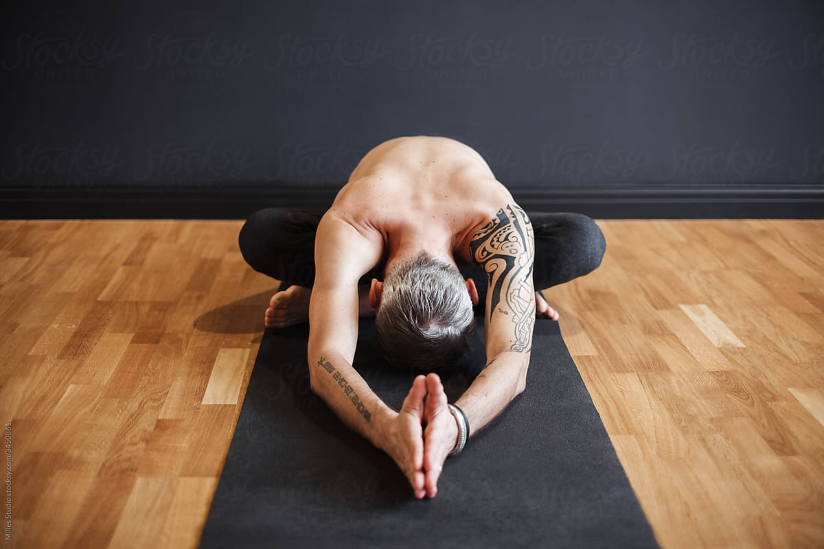 Unrecognizable shirtless male bending forward and meditating