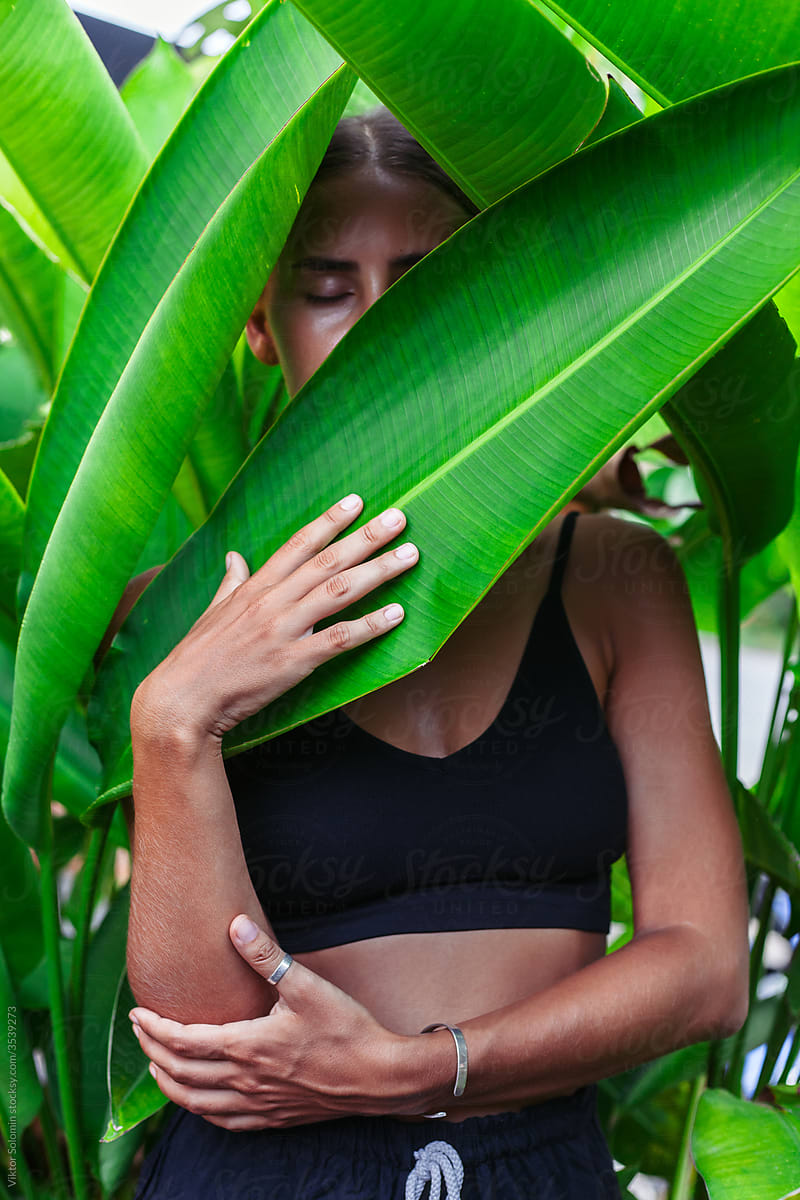 Anonymous slim woman hiding behind exotic banana leaf
