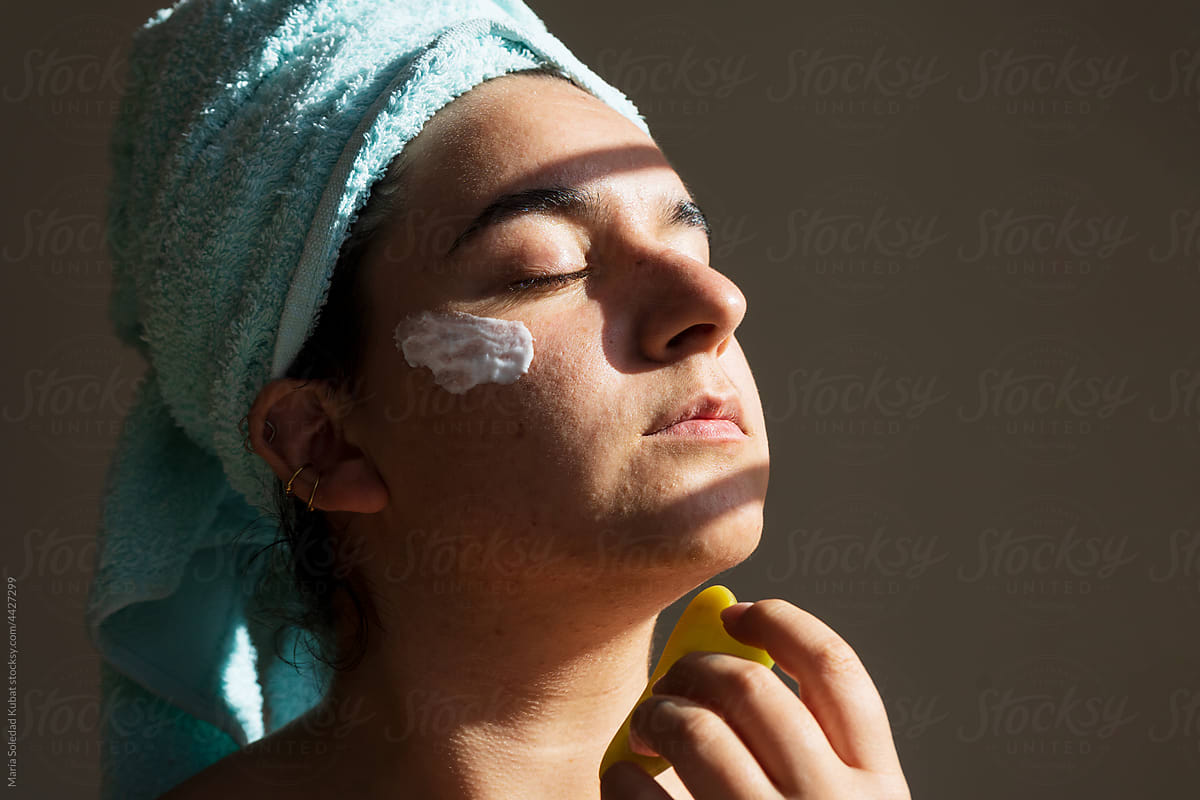 Young woman treating face with gua sha massage at home