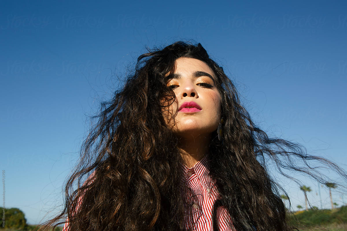 Young girl with long black curly hair posing under the blue sky