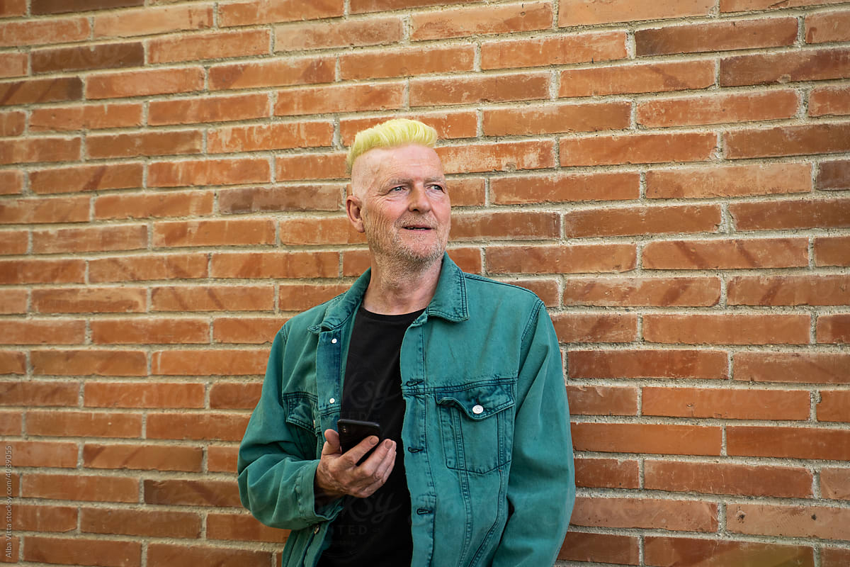 Cool senior man standing in front of wall with phone