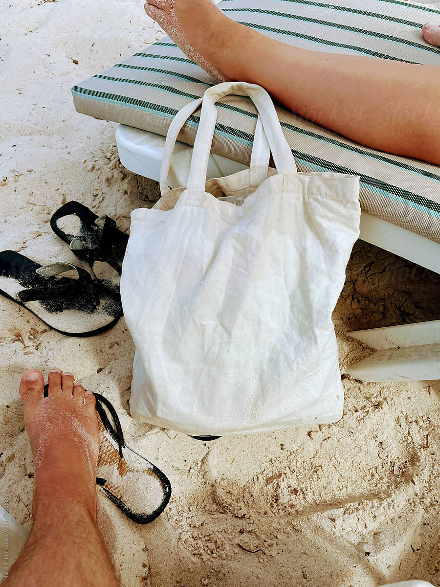 White tote bag lying on a beach next to a sunbed