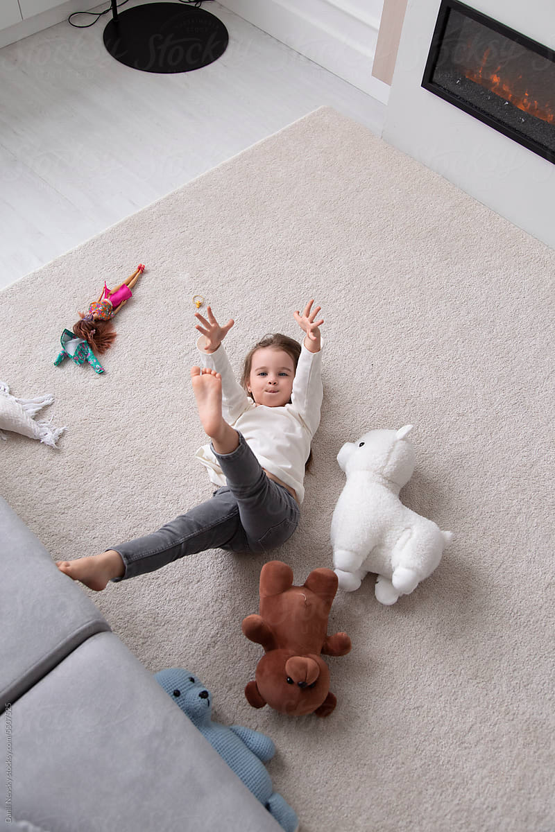 Carefree child having fun on rug with toys