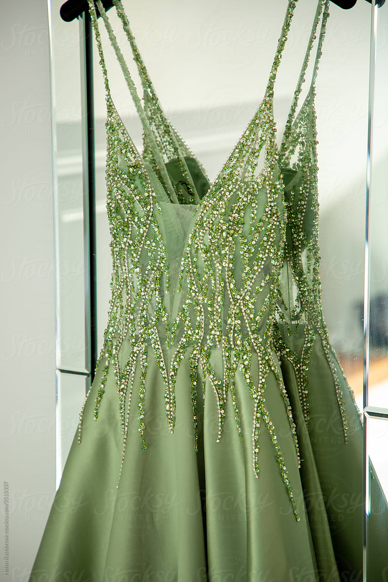 Green beaded formal dress hanging in a bedroom.