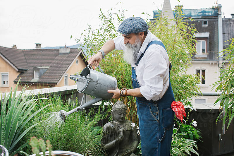 Outdoor Portrait of Elderly Male Hipster Using Watering Can on R
