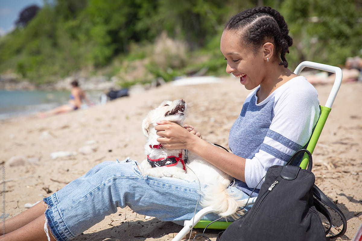 Teenager looking at her pet dog as she lounges on a beach chair