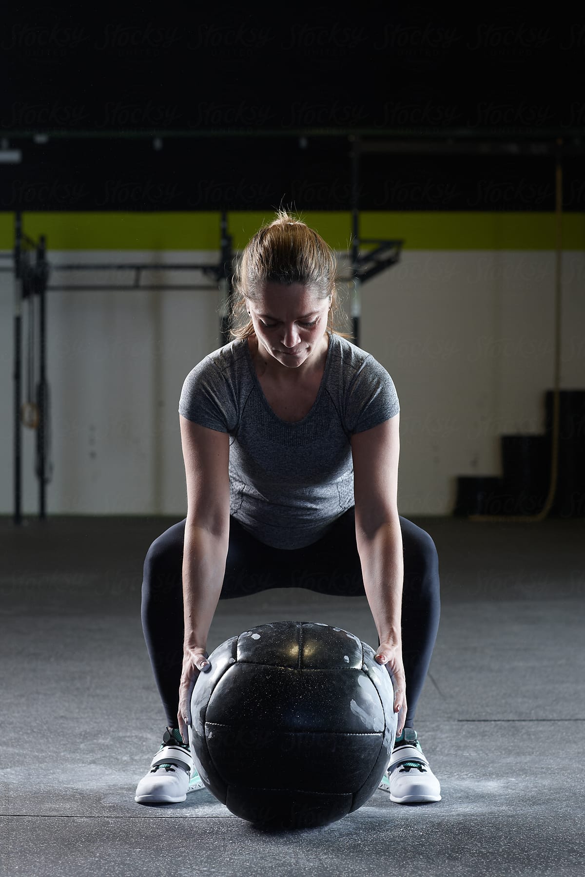 Fit woman positioning to lift heavy ball for workout