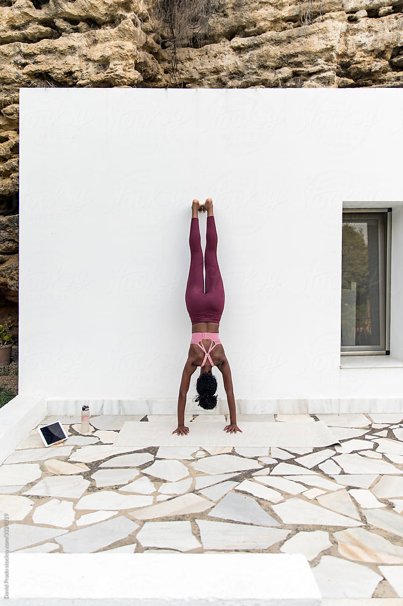Anonymous ethnic female doing handstand near wall