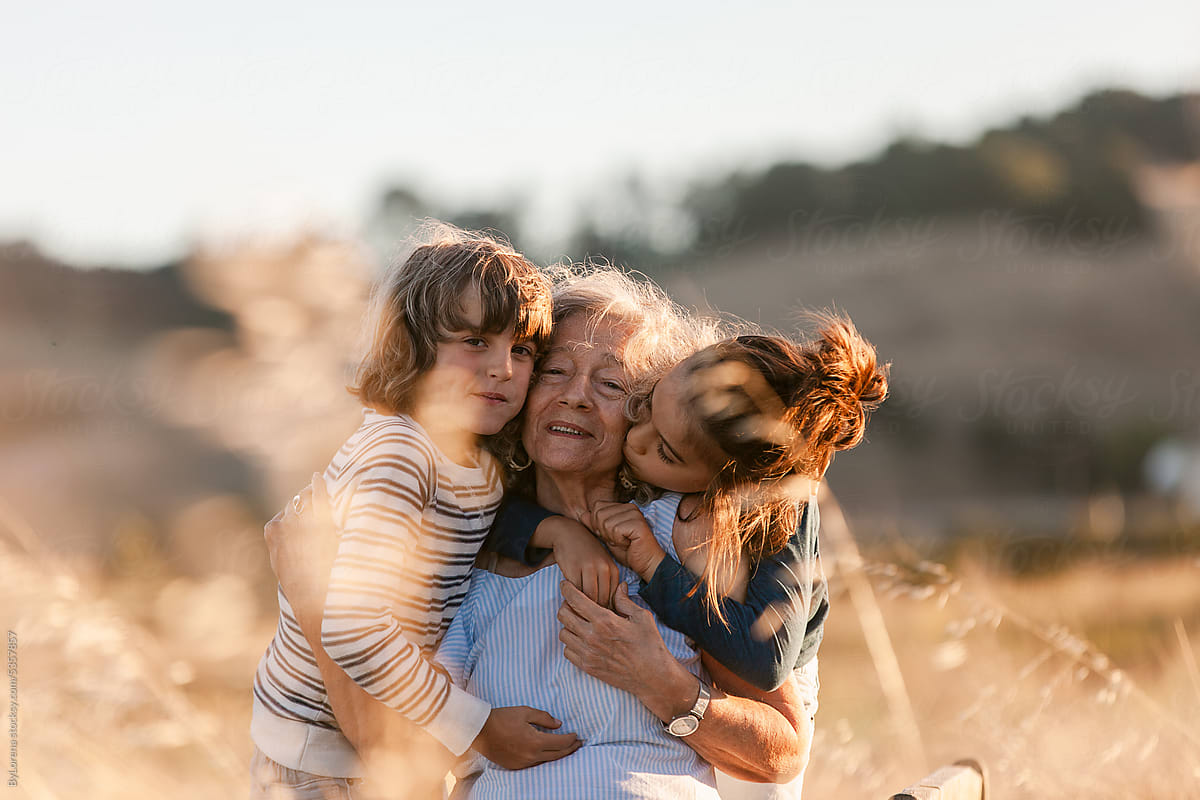 Kids kissing their grandma together surrounded by nature