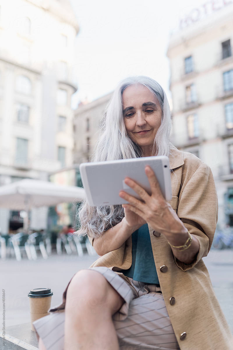 Grey-haired woman  sitting in the street using a tablet