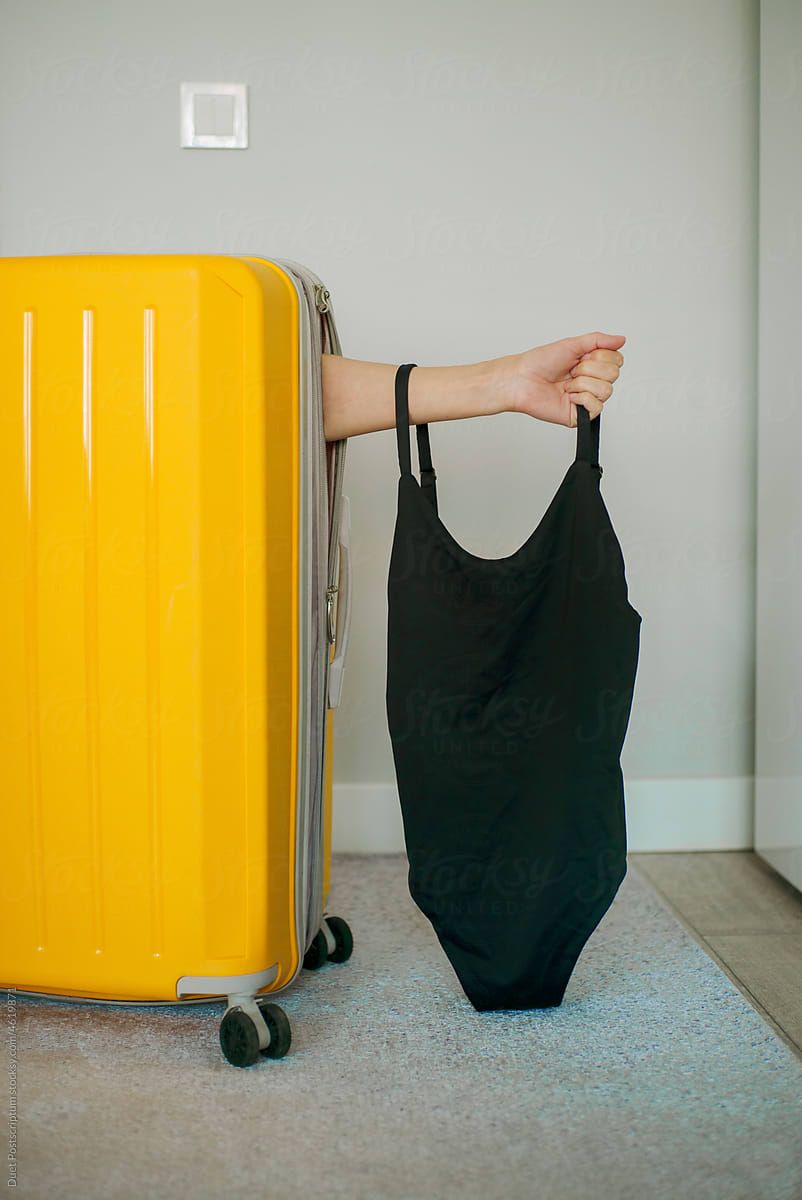 An unrecognizable person packed into a travel suitcase with swimsuit