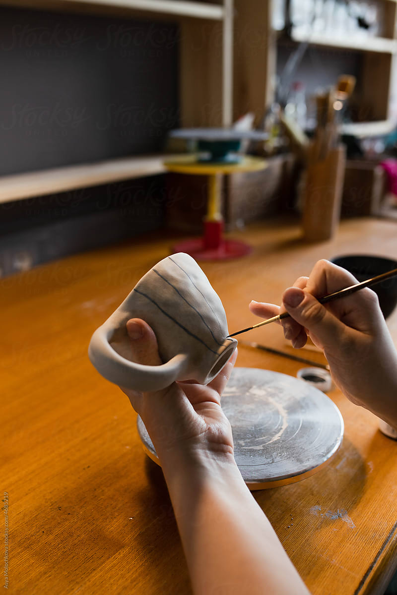 Young woman ceramist applying paint to clay mug