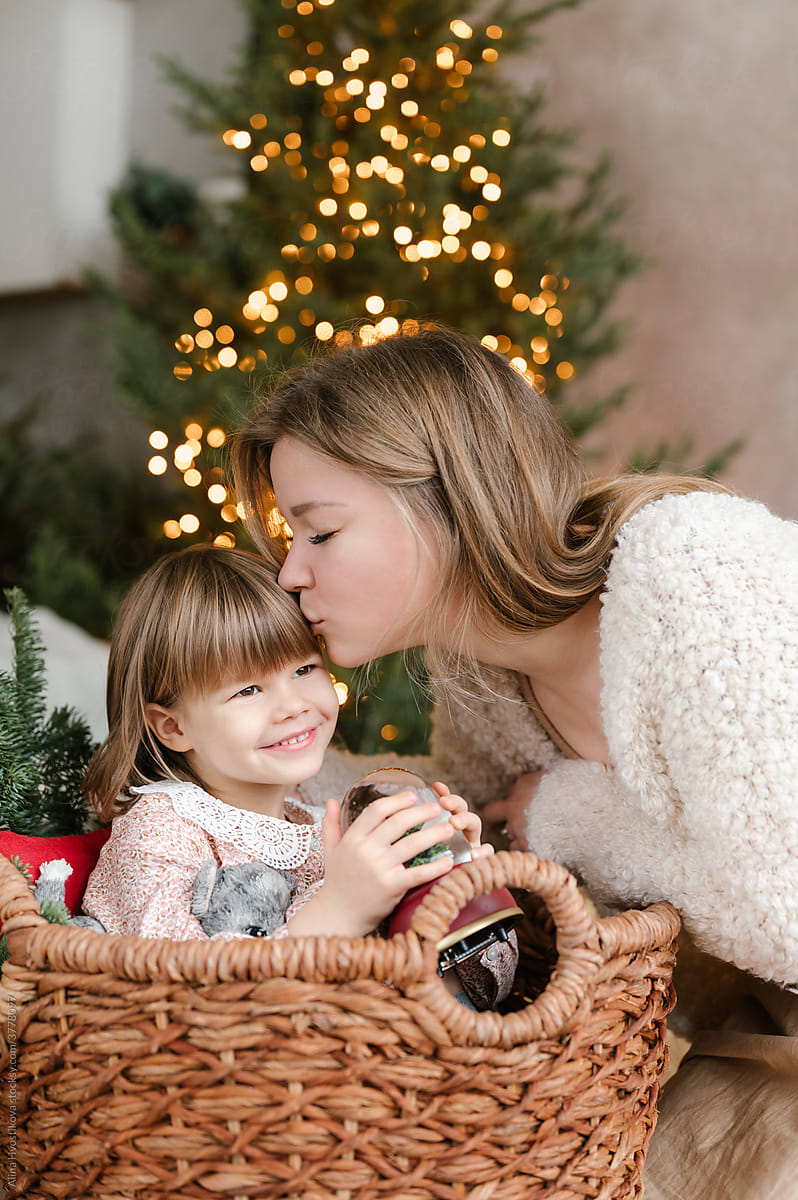 Loving mother kissing girl in wicker basket during Christmas