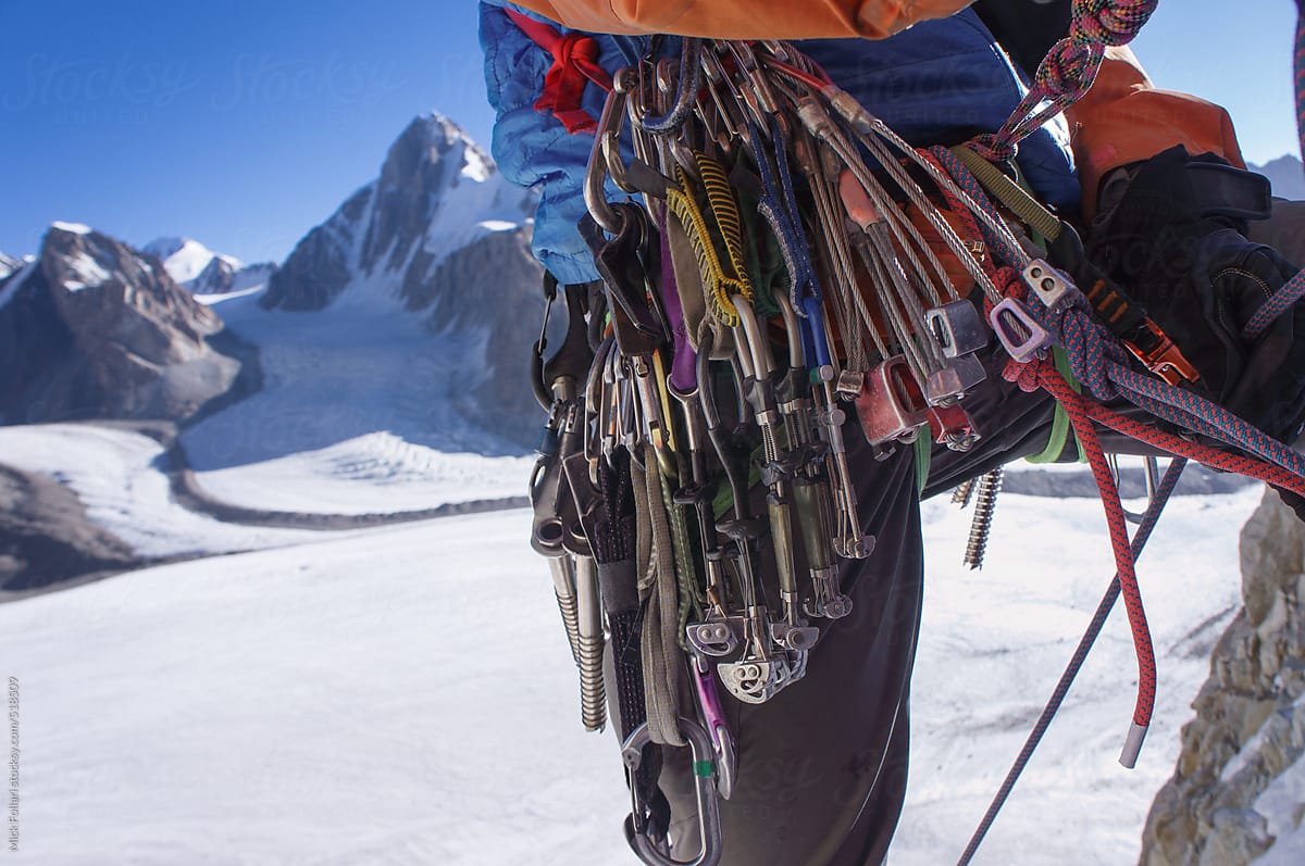 Traditional ice and rock climbing gear on a harness in the alpine mountains with glacier behind