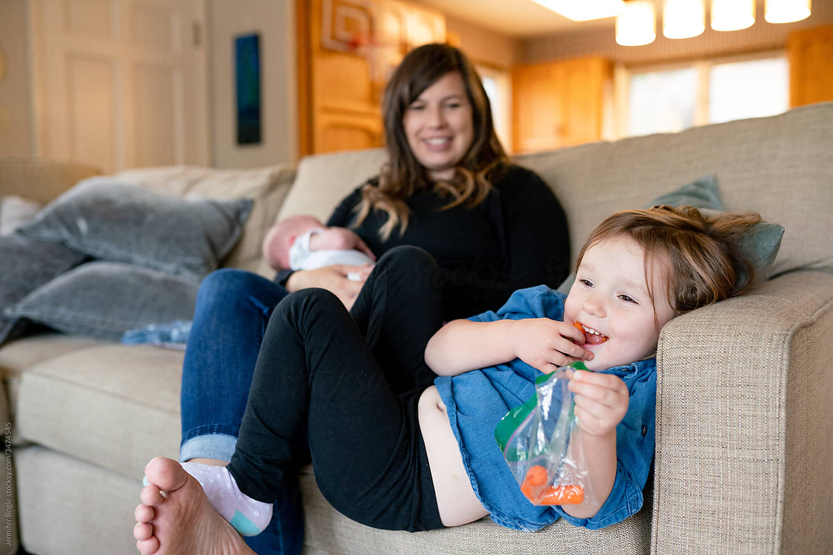 Toddler eats carrots while mom holds infant