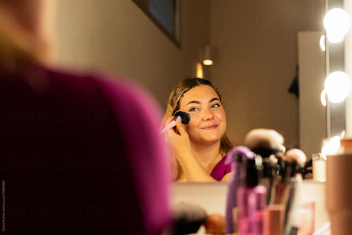 smiling teen girl Applying Blush in a vanity mirror