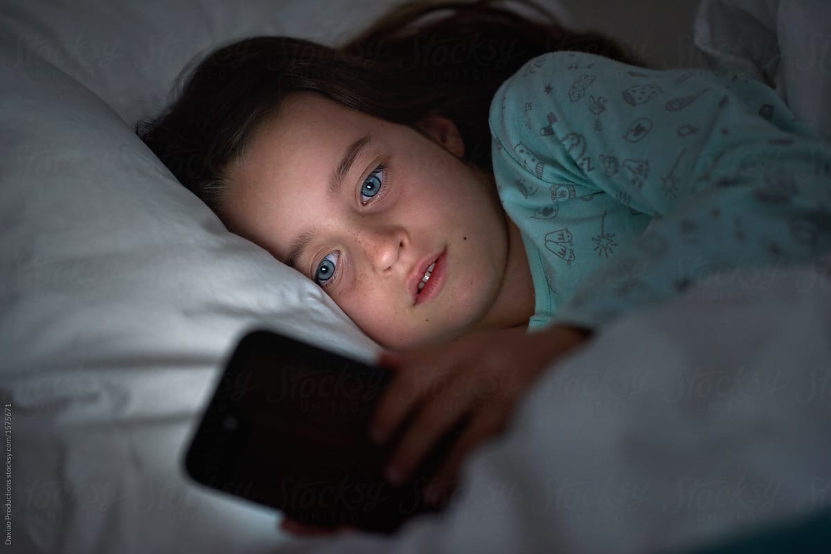 Young girl playing with phone in dark bedroom