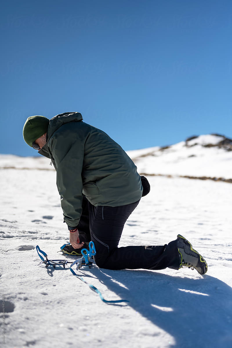 Hiker putting on crampons in snowy mountains