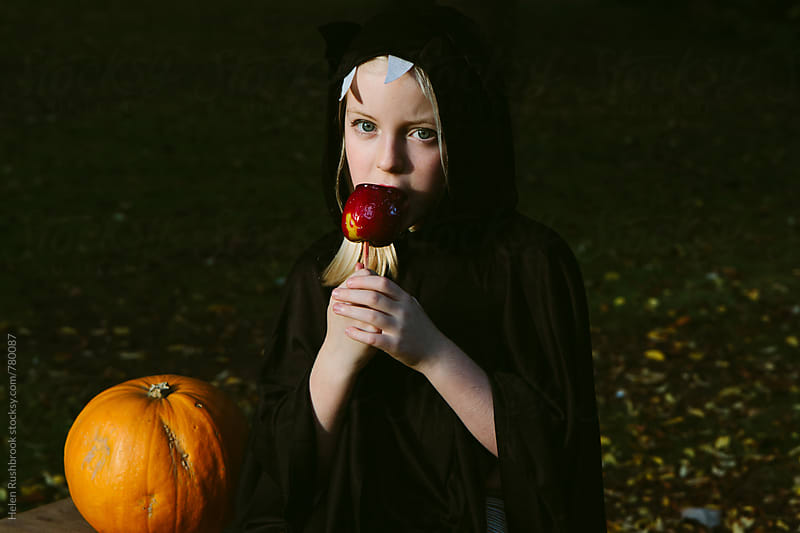 A little girl dressed as a bat eating a toffee apple.